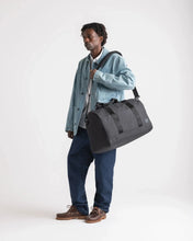 Load image into Gallery viewer, A young man holding the duffle bag with the strap on his shoulder. Set on a light gray background.