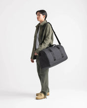 Load image into Gallery viewer, A young woman carrying the duffle bag on her shoulder. Set on a light gray background.