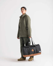 Load image into Gallery viewer, A young woman holding a black and tan 40 Liter duffle bag.