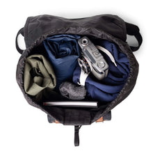 Load image into Gallery viewer, Top interior view of the backpack opened with clothes and accessories folded inside.
