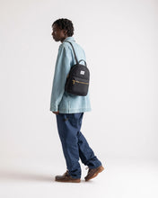 Load image into Gallery viewer, A young man facing left while carrying the black mini backpack.