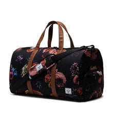 Load image into Gallery viewer, Angled view of the black duffle bag with floral print, brown grab handles, and an adjustable shoulder strap.