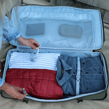 Load image into Gallery viewer, Within the green duffle bag, a pair of hands secures the clothes and accessories in the main compartment.