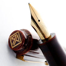 Load image into Gallery viewer, Angled close up to the fountain pen nib leaning on the top of the cap. Set on a white background. The nib is golden in color, and features an engraving of the AP logo, and a B for broad point.