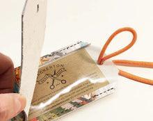 Load image into Gallery viewer, Product packaging with a brand label and orange strap on a white background