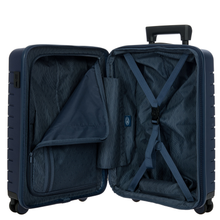 Load image into Gallery viewer, Opened view of the suitcase on a white background. The lining is blue, the lid's side features a zipper-close compartment, and the back side has a set of straps and a small pouch to keep items in place.