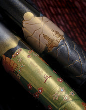 Load image into Gallery viewer, Close up to the artist signature on the barrel, and the buildings of the cap. Set on a brown background.