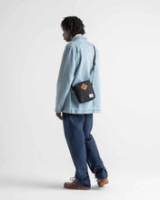 Load image into Gallery viewer, A young man dressed in blue, carrying the black cross body bag.