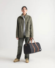 Load image into Gallery viewer, A young woman holding a black novel duffle bag by the grab handles.