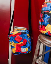 Load image into Gallery viewer, The colorful crossbody bag hanging from a red shelf.