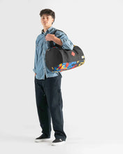 Load image into Gallery viewer, A young man holding the black Herschel Lego duffle bag on a light gray background.