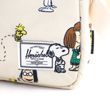 Load image into Gallery viewer, Close up to the Herschel logo tag at the bottom front right corner of the bag. It features a stitched Snoopy and Woodstock on the sides.