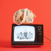 Load image into Gallery viewer, The crossbody bag set on top of a TV with a Peanuts group shot on a red background.