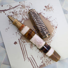 Load image into Gallery viewer, The pen with the cap removed, laying on the included booklet and presentation box.