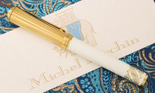 Load image into Gallery viewer, Side view of the fountain pen with the cap on. Set on top of the certificate and a blue embroidered fabric.