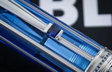 Load image into Gallery viewer, Close-up of the blue gemstone, shown against a dark background with blurred white letters.