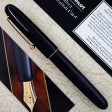 Load image into Gallery viewer, Side view of the black fountain pen arranged on top of the outer box with the included pamphlets.