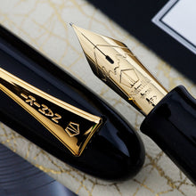 Load image into Gallery viewer, Close up to the fountain pen nib and cap. They're both golden and engraved wit the Namiki logo. The nib has the mount Fuji engraved in its design, along with the text: 18K-750, <F>. The point of your nib will vary on availability.