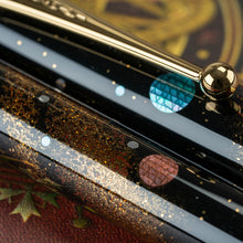 Load image into Gallery viewer, Angled close up to the pen's barrel and cap. The high craftsmanship on the circle-shaped cuts of the raden composing the planets can be appreciated. One is blue, the other one a soft red, almost pink.
