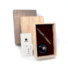 Load image into Gallery viewer, View of the Fountain Pen set on its resting place with the ink bottle on the wooden presentation box. The outer box is shown with the care booklet, and the artist signature card.