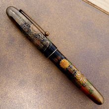 Load image into Gallery viewer, Side view of the Fountain Pen with the cap on, placed on top of the outer box. It is a soft brown color with some shimmering specks of gold color painted on the surface.