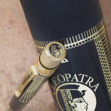 Load image into Gallery viewer, Close up to The Retro 51 Cleopatra rollerball pen's top disk leaning on the black gift tube. The top disk is decorated with a profile icon of Cleopatra's face.