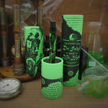 Load image into Gallery viewer, The pen placed on the bottom portion of the gift tube with the caps arranged around it with themed accessories.