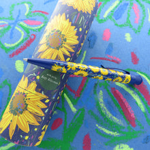 Load image into Gallery viewer, The pen leaning on the gift tube. Set on a blue background with sketches made in oil pastel.