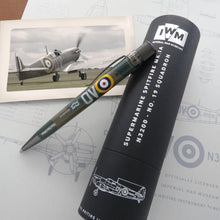 Load image into Gallery viewer, Side view of the Retro 51 Spitfire N3200 rollerball pen leaning on it gift tube. The background has a print with schematic and a picture of the plane.