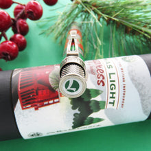 Load image into Gallery viewer, The Retro 51 Limited Edition Lionel Trains Christmas Light Express sits atop the presentation tube showing the top disc of the rollerball pen, it is the letter "L" for Lionel Trains, the lettering is white with a green background.