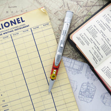 Load image into Gallery viewer, Front view of the rollerball pen. Laid on different papers with printed graphics and a small book.