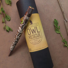 Load image into Gallery viewer, The Retro 51 Owl Rescue Rollerball Pen resting on the presentation gift tube on a textured brown background with leaves.