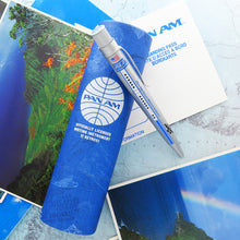 Load image into Gallery viewer, The rollerball pen leans on its blue presentation tube. The background is a set of postcards.