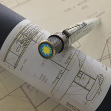 Load image into Gallery viewer, A close-up of the pen resting on its presentation tube, with the pen featuring a circular blue and yellow sun emblem on its cap.