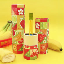 Load image into Gallery viewer, A yellow and green pen displayed in a colorful fruit themed gift tube with two tubes behind it. It is arranged on a yellow background with bananas.