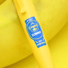 Load image into Gallery viewer, Close up to the blue sticker design on the yellow pen with an icon of a monkey with sunglasses and text: #1951 YUMMY Go Bananas