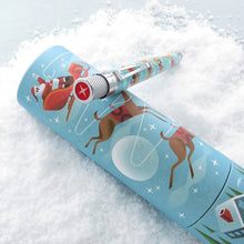 Load image into Gallery viewer, Angled top view of the Christmas themed pen leaning on the matching gift tube on a snowy background.