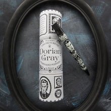 Load image into Gallery viewer, The Picture of Dorian Gray by Oscar Wilde themed pen and gift tube displayed inside a black oval frame on a dark textured blue background.