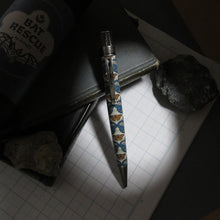 Load image into Gallery viewer, Front view of the pen, arranged on a paper grid background, a rock and black notebooks.