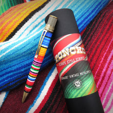 Load image into Gallery viewer, The sarape style rollerball displayed on top if its presentation tube on a sarape texturized background.