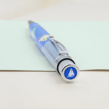 Load image into Gallery viewer, Angled top disk view of the pen. It has white and blue icon of a sailboat.