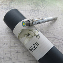 Load image into Gallery viewer, The Retro 51 Spirit of St. Louis Rollerball Pen leaning on its matching gift tube. The background is a printed world map.