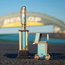 Load image into Gallery viewer, Side view of the pen in its trophy stand with the lit lighter and cufflinks. Set on a race track background.