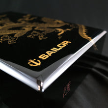 Load image into Gallery viewer, Angled close up to the Sailor logo painted on the bottom left of the lid. The artist signature is visible on the front face of the box lid.