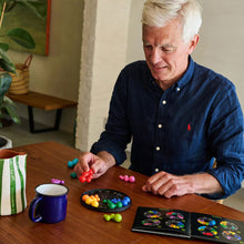 Load image into Gallery viewer, Man playing a board game with colorful pieces on a wooden table.