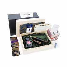 Load image into Gallery viewer, Arrangement of all the contents on a white background. The black cardboard box, a white Taccia card, a wooden presentation box, a cartridge converter, two blue ink cartridges, an ink bottle with its box, a rectangular origami paper, a printed certificate, a small card showing different inks, a kimono sleeve, and the fountain pen.