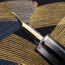 Load image into Gallery viewer, Close-up of the side of the fountain pen nib on a textured surface. The nib is engraved with a small M for medium point.