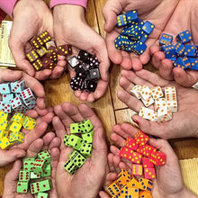 Load image into Gallery viewer, Hands holding different sets of colorful dice on a wooden surface.