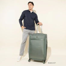 Load image into Gallery viewer, A young man posing while holding the green suitcase by the extended telescopic handle.
