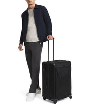 Load image into Gallery viewer, A young man holding the black suitcase's telescopic handle.